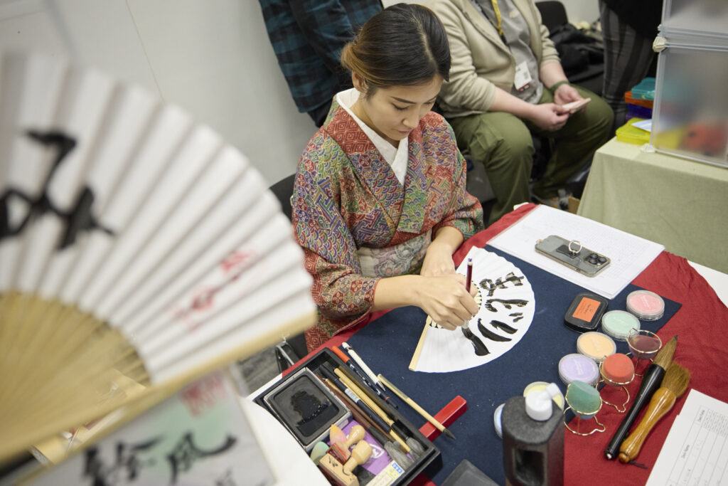 Foto von einer Künstlerin, die Japanische Fächer mit Kalligraphie-Schriftzeichen betuscht