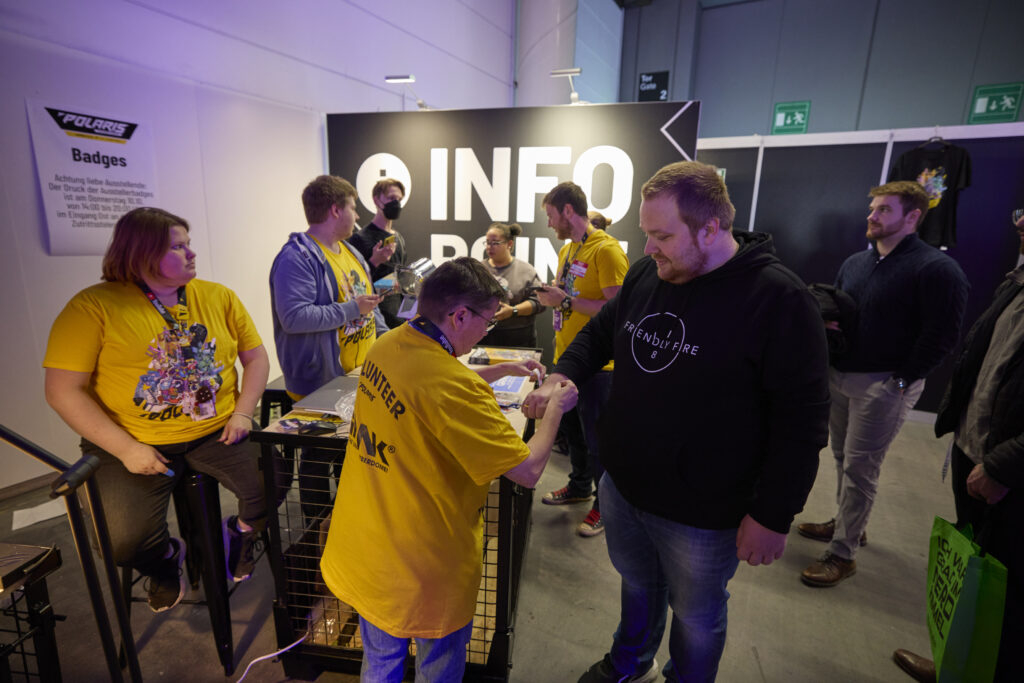 Foto vom Infostand der POLARIS Convention 2024. Einem Gast wird ein Tyvek-Band angelegt.